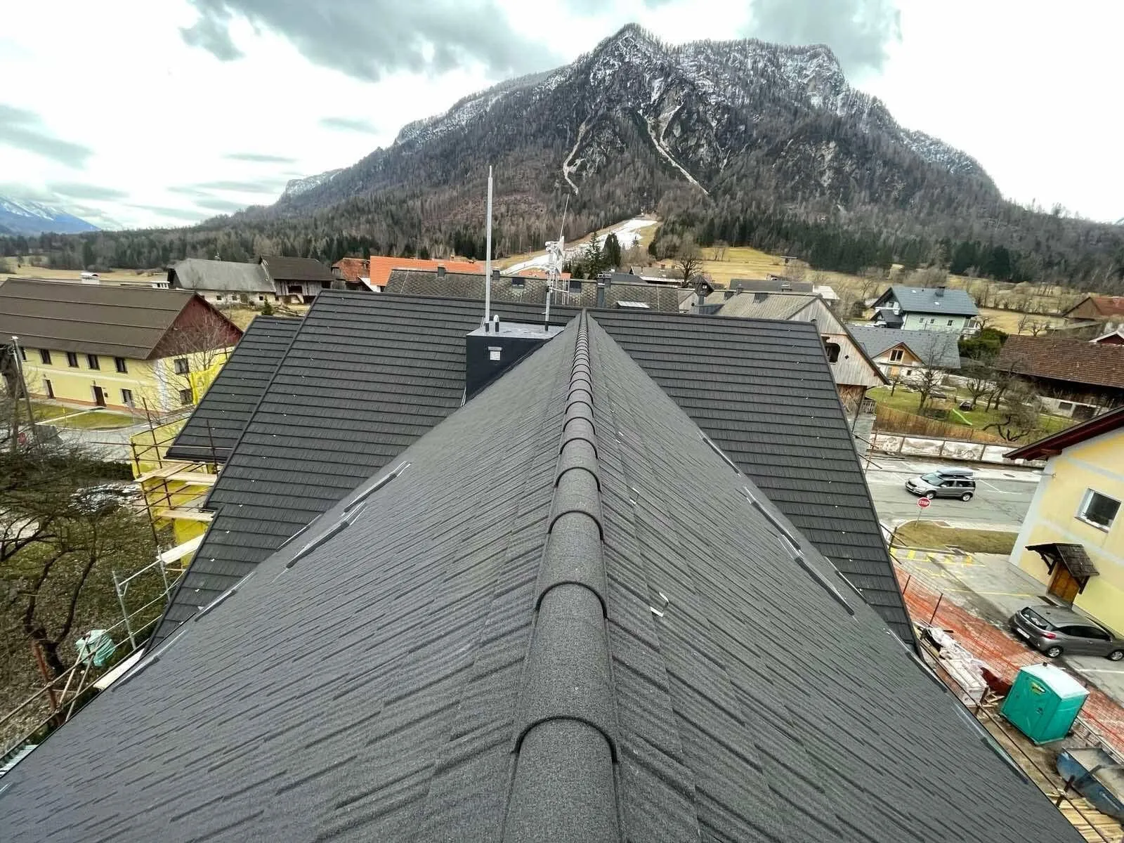 Sveže prekrita streha z opečno kritino nad slovensko vasjo, v ozadju gore